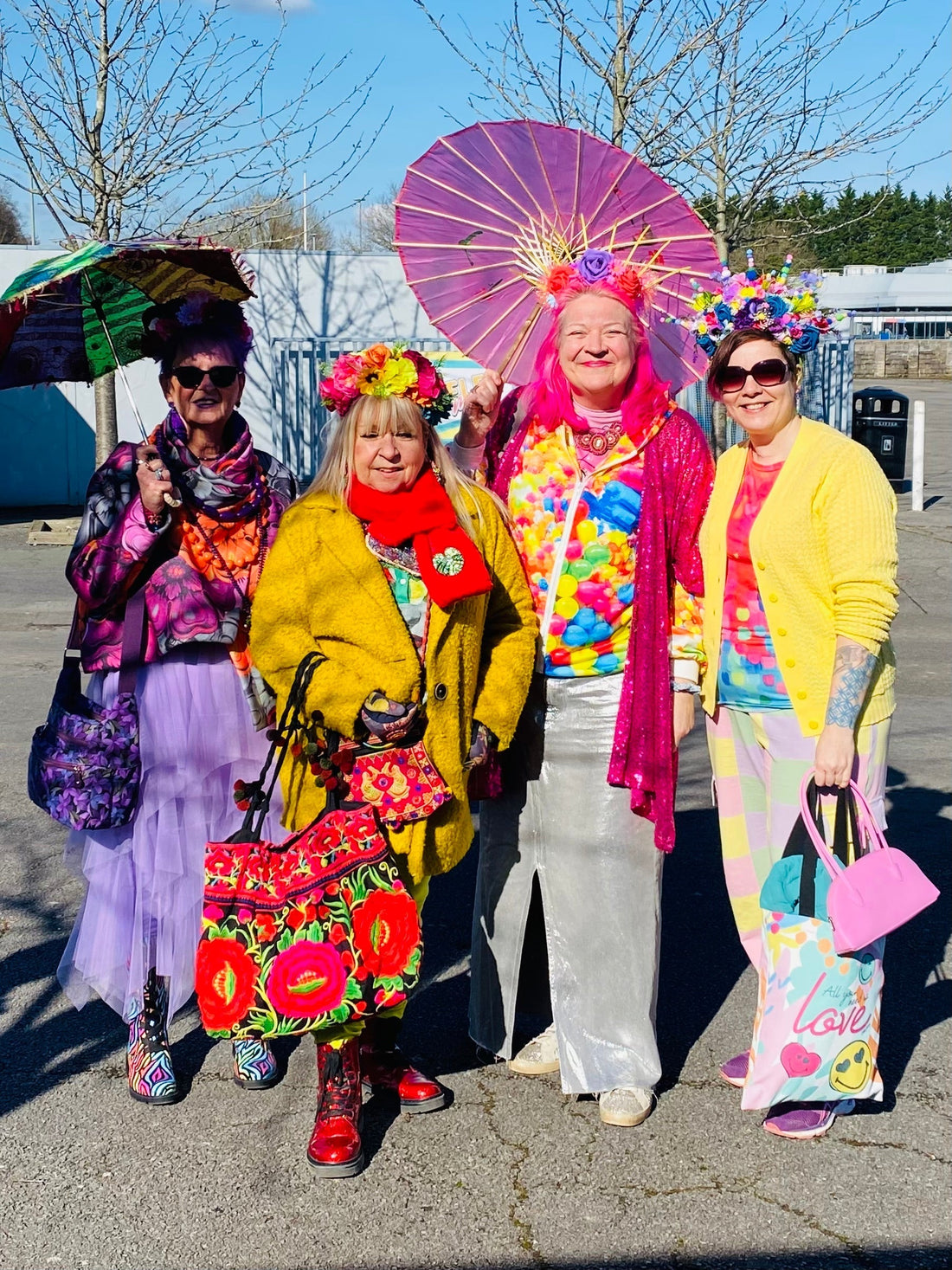 4 vibrant ladies wearing colourful outfits and carrying vibrant parasols and handbags