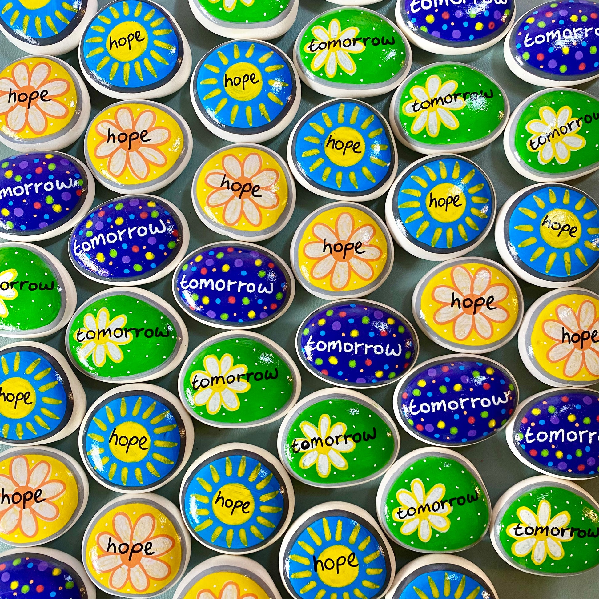 Lots of Yellow, Green, and Blue Hand painted pebbles with the words Hope and Tomorrow written on