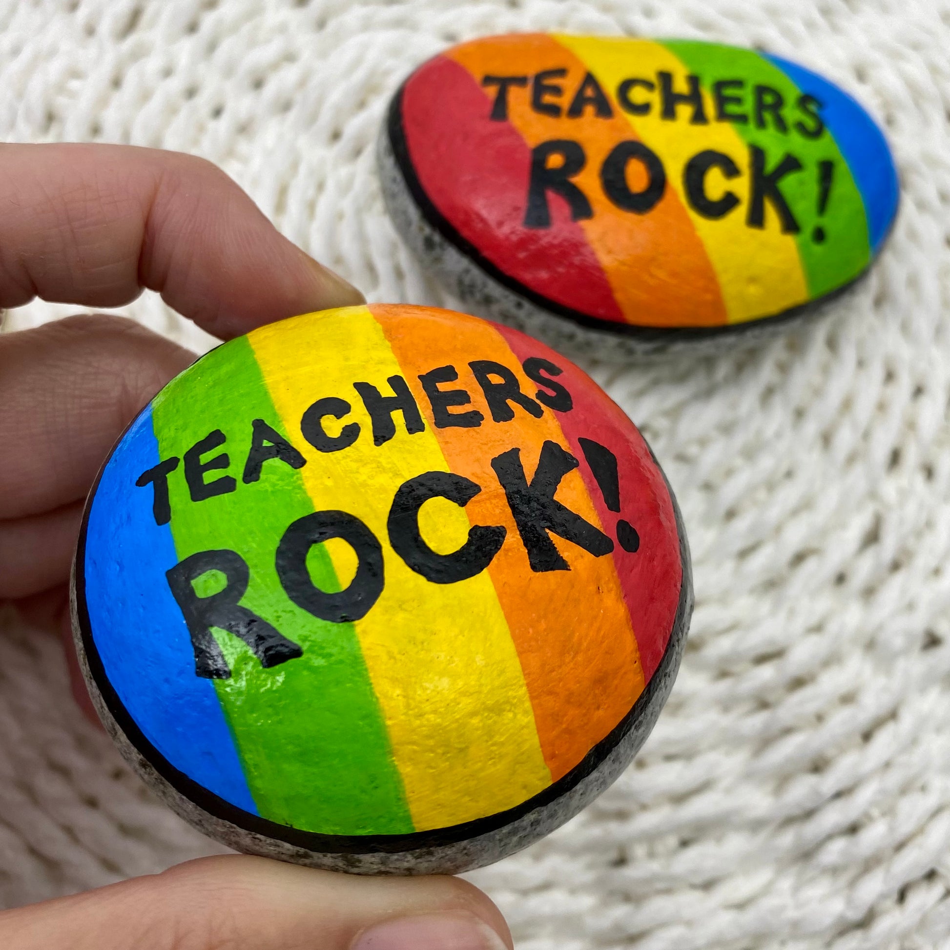 2 rocks painted with bright rainbow stripes and the words"Teachers Rock" written on.