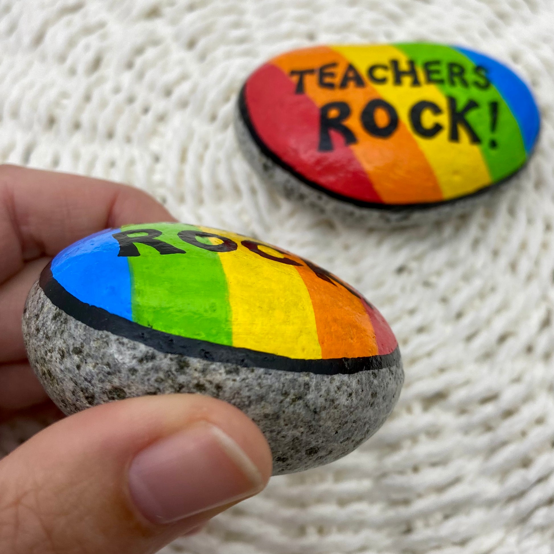 2 rocks painted with bright rainbow stripes and the words"Teachers Rock" written on.