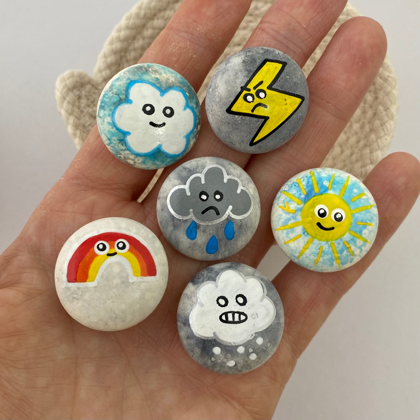6 small hand painted weather themed pebbles held in a hand