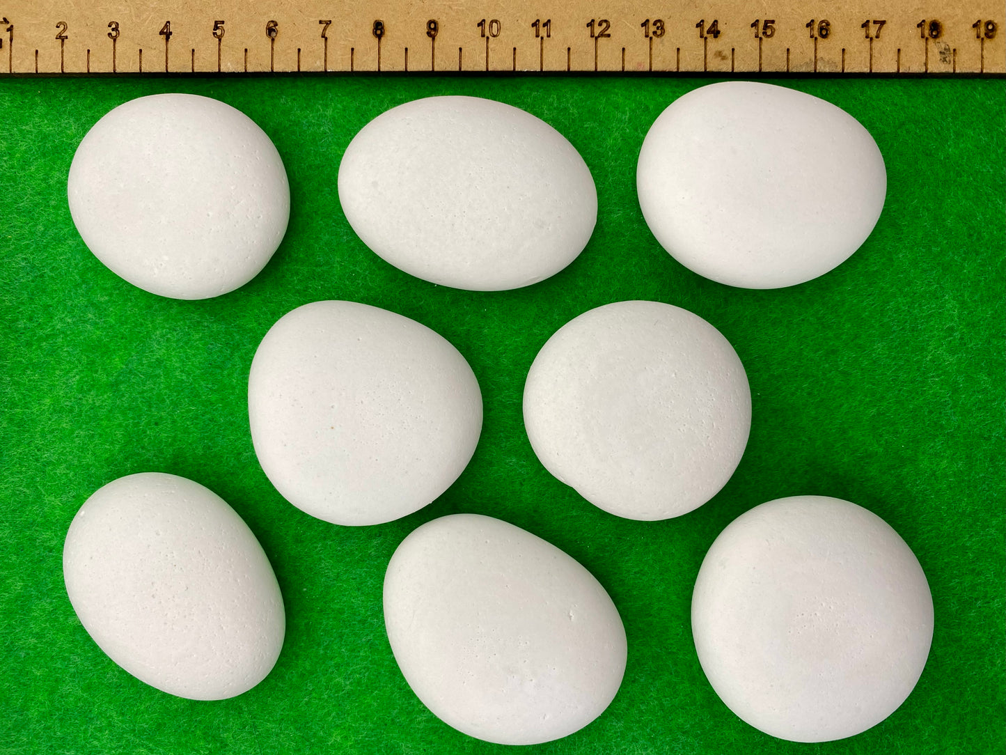 8 small white plaster pebbles of different shapes and sizes next to a ruler