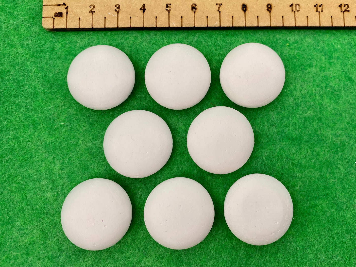 8 tiny white circular plaster pebbles next to a ruler