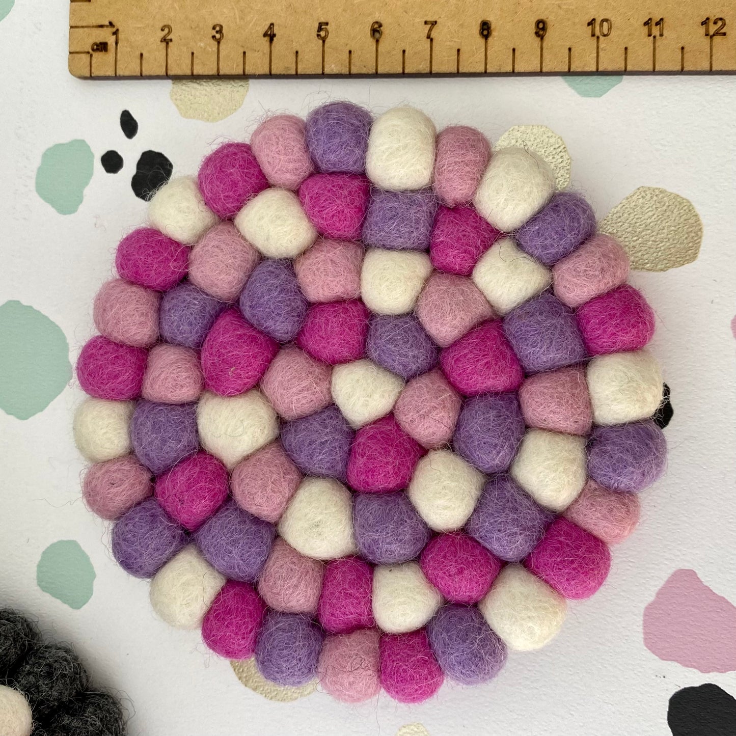 Colourful Coaster sized Mat made from Felt Balls in Pink, Purple and White. Next to a ruler