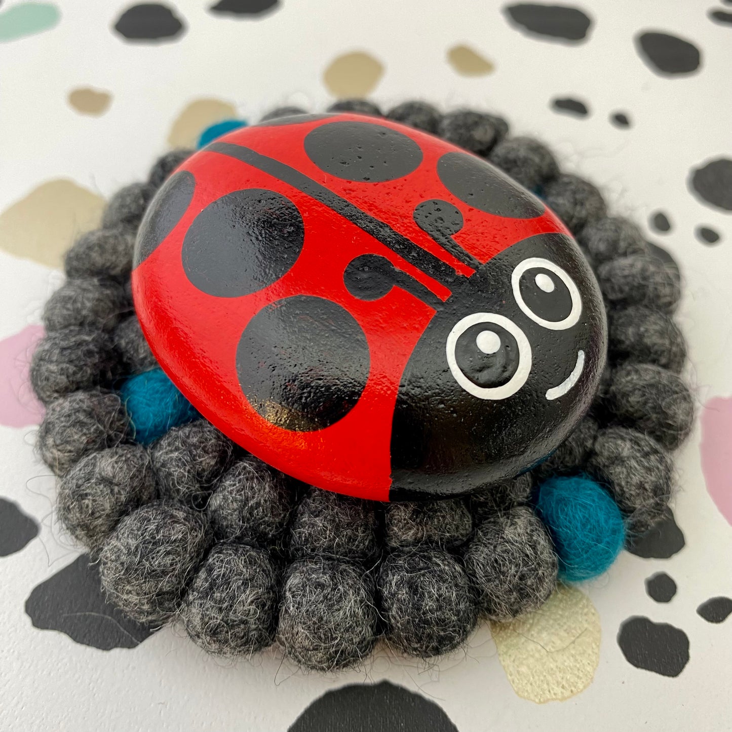 Coaster sized Mat made from Grey and Blue Felt Balls with a Hand painted Ladybug Pebble on top