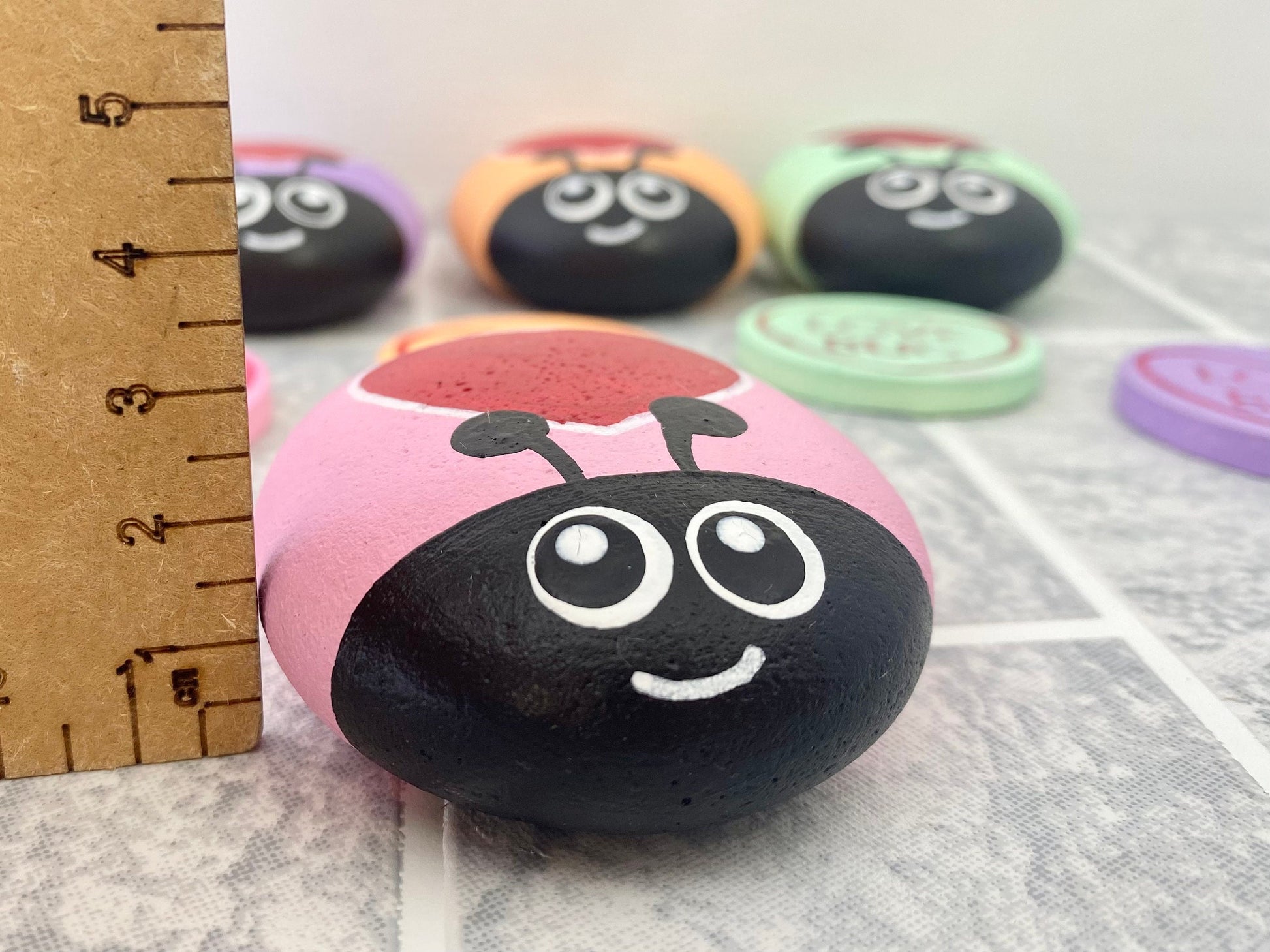 Hand painted Pink Pastel Heart Bug Pebble next to a ruler